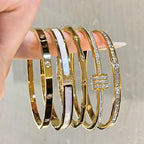 Set of gold bangles with diamond accents on a hand against a neutral background