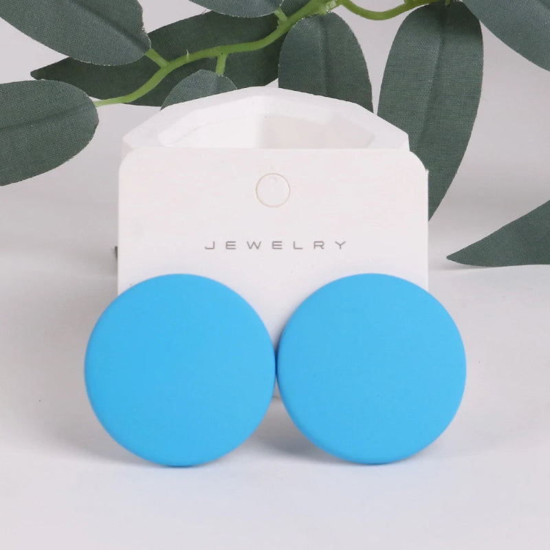 Blue round earrings on a jewelry card with green leaves in the background