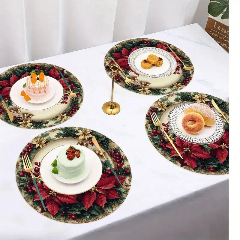 Three round Christmas-themed placemats with red poinsettias, green holly, gold bows, and white plates are arranged on a white tablecloth. Each placemat is styled with a white plate, gold cutlery, and a small dessert or pastry.