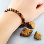 Hand wearing a tiger eye bracelet with tiger eye stones on a light gray background