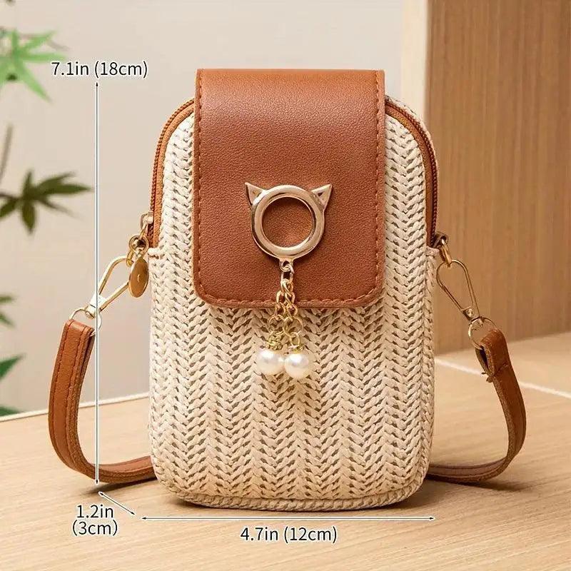 Small woven handbag with brown leather top and cat-shaped keychain on a wooden surface.