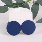 Blue round earrings on a white jewelry card with green leaves in the background