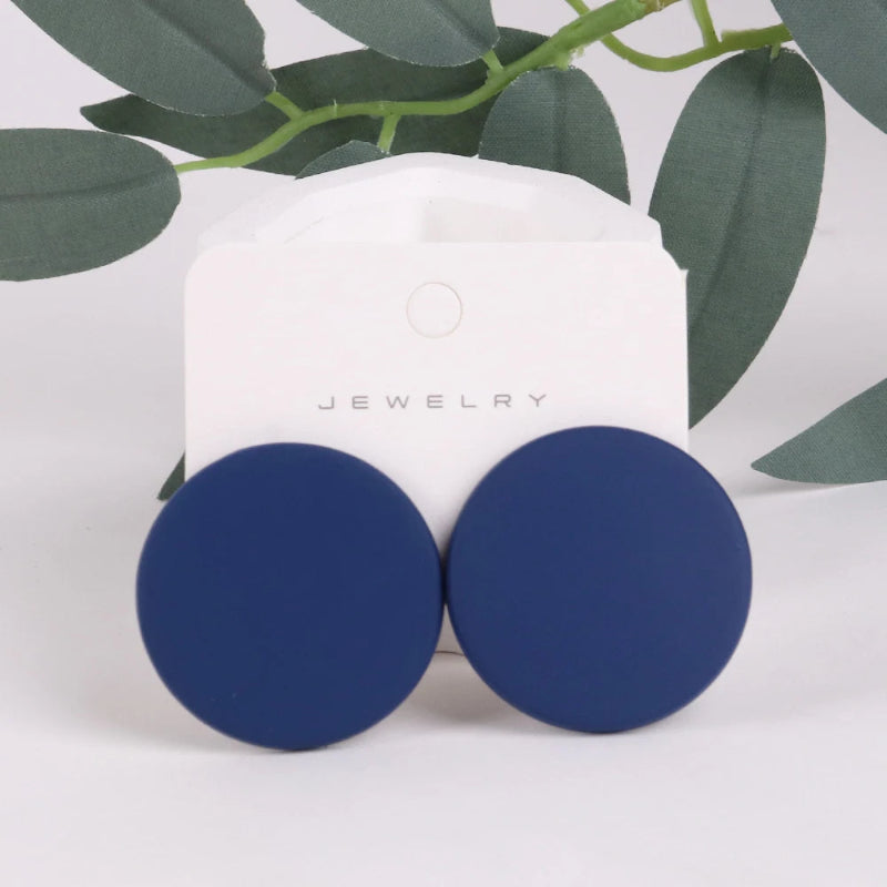 Blue round earrings on a white jewelry card with green leaves in the background