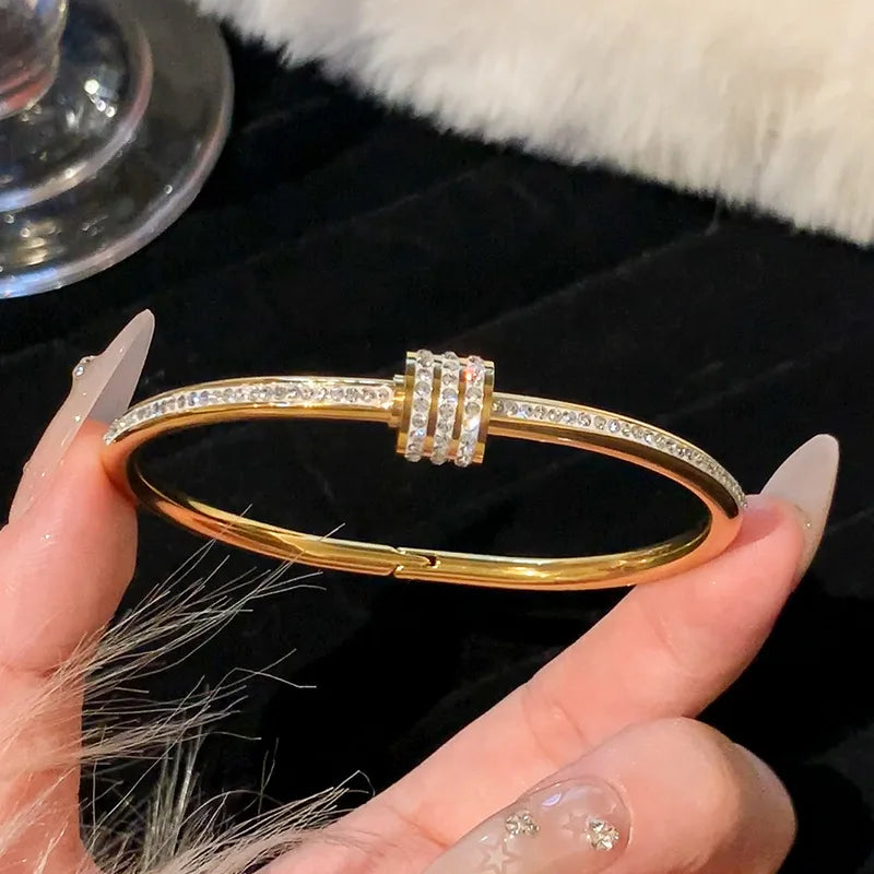 Gold bracelet with diamond accents held by a hand against a black background