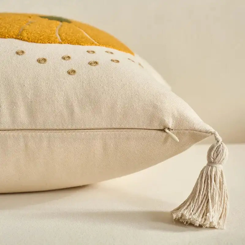 A close-up of a cream-colored decorative throw pillow with a tassel and embroidered details, featuring a mustard yellow textured section near the top.