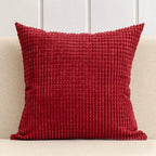 Red textured pillow on a beige couch with a white paneled wall background