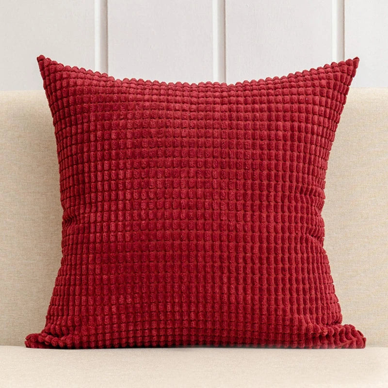 Red textured pillow on a beige couch with a white paneled wall background
