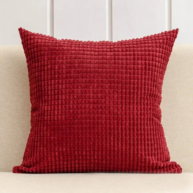 Red textured pillow on a beige couch with a white paneled wall background