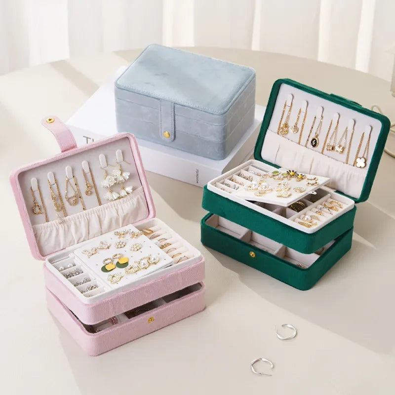 Three jewelry boxes in pink, green, and white with jewelry inside on a light background.