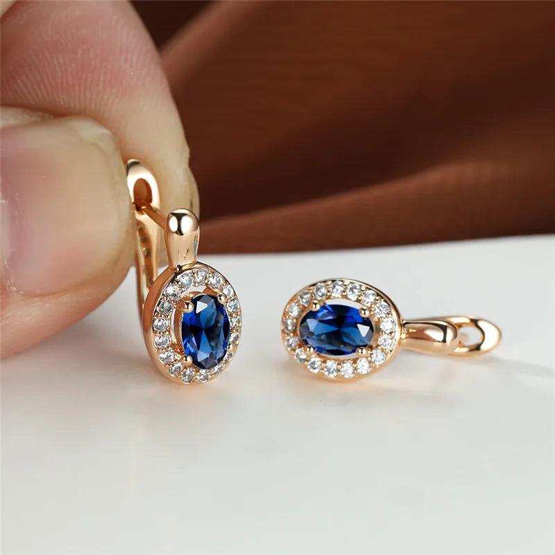 Gold earrings with blue gemstones held by a hand on a neutral background