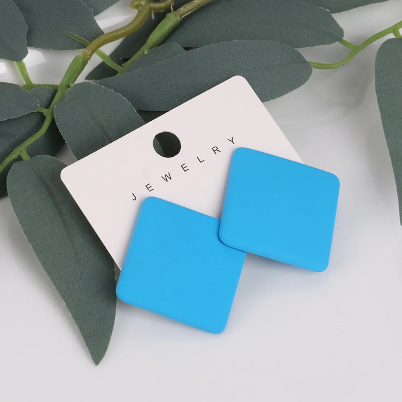 Blue square earrings on a white jewelry card with green leaves in the background