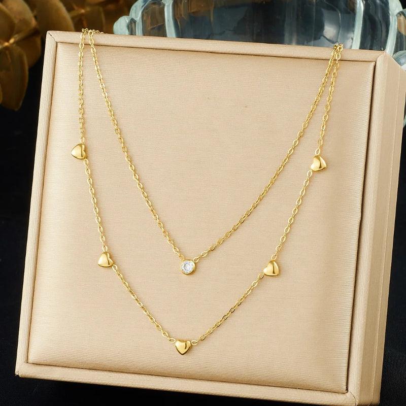 Gold necklace with heart-shaped pendants on a beige display box.