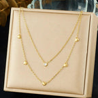 Gold necklace with heart-shaped pendants on a beige display box.