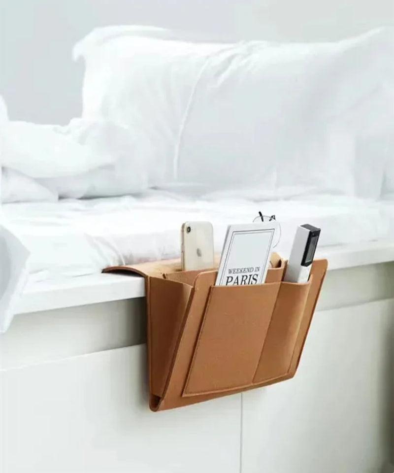 Brown magazine holder attached to a white bed with books and a phone inside.