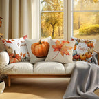 Four autumn-themed throw pillows arranged on a white sofa in a bright living room. The pillows feature watercolor-style pumpkins, orange maple leaves, and the words 'Hello Pumpkin' and 'Thankful.