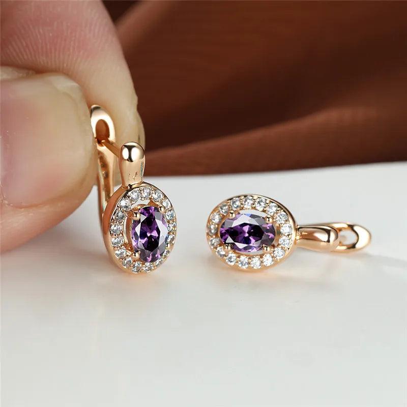 Rose gold earrings with purple gemstones held by a hand on a neutral background