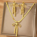 Gold bow-shaped necklace and earrings on a beige background