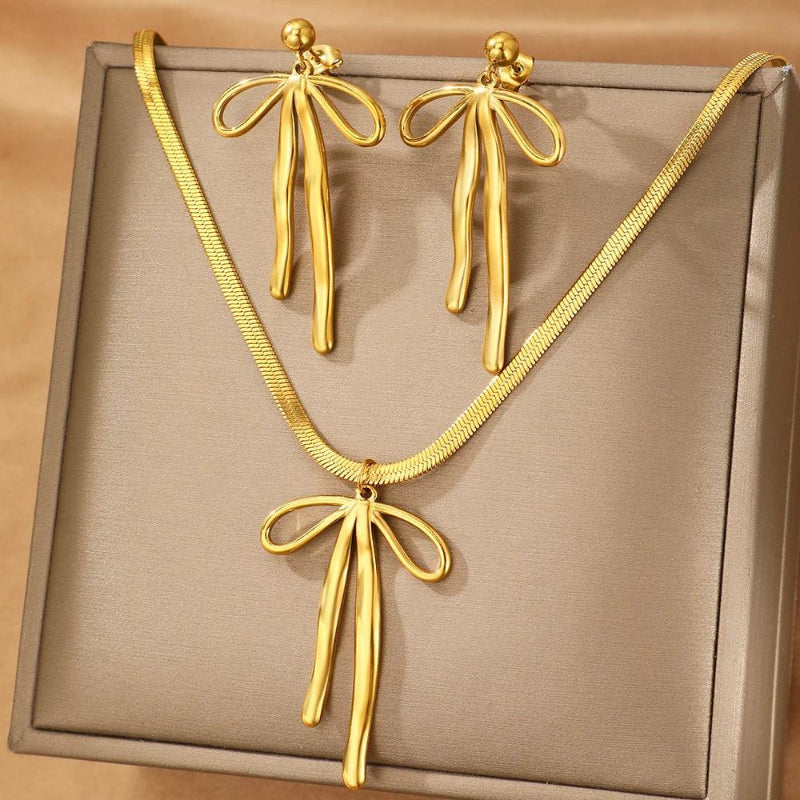 Gold bow-shaped necklace and earrings on a beige background