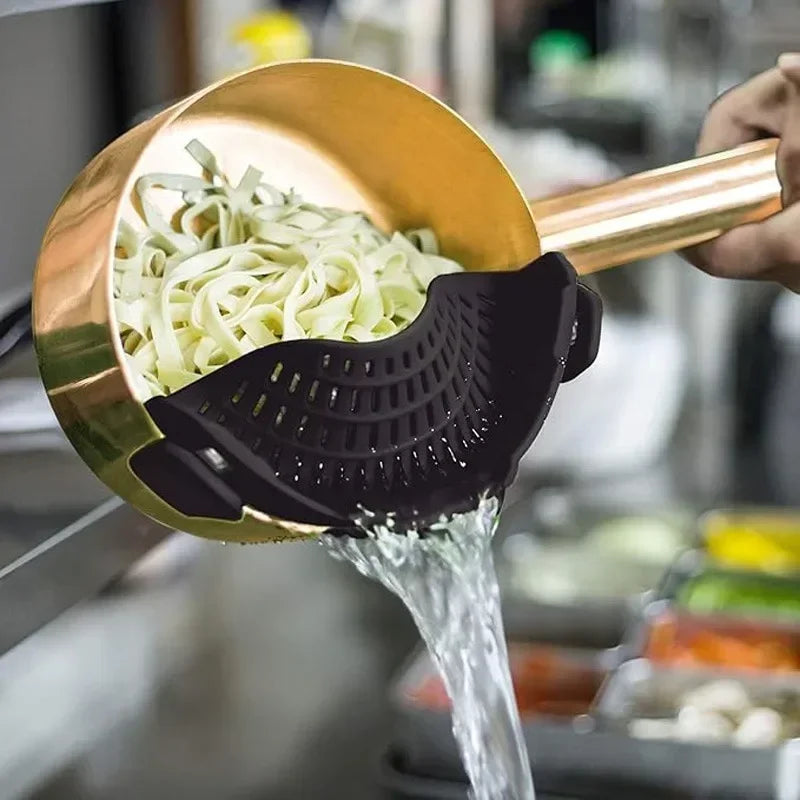 Copper-colored ladle with a black silicone scoop pouring water over noodles in a kitchen setting.