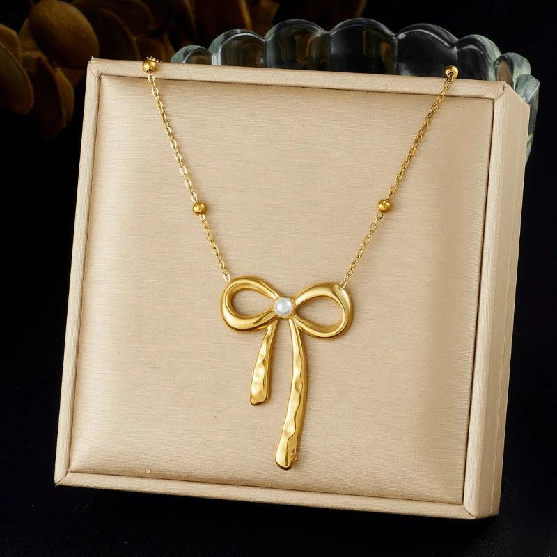 Gold bow-shaped necklace on a beige display box with a dark background