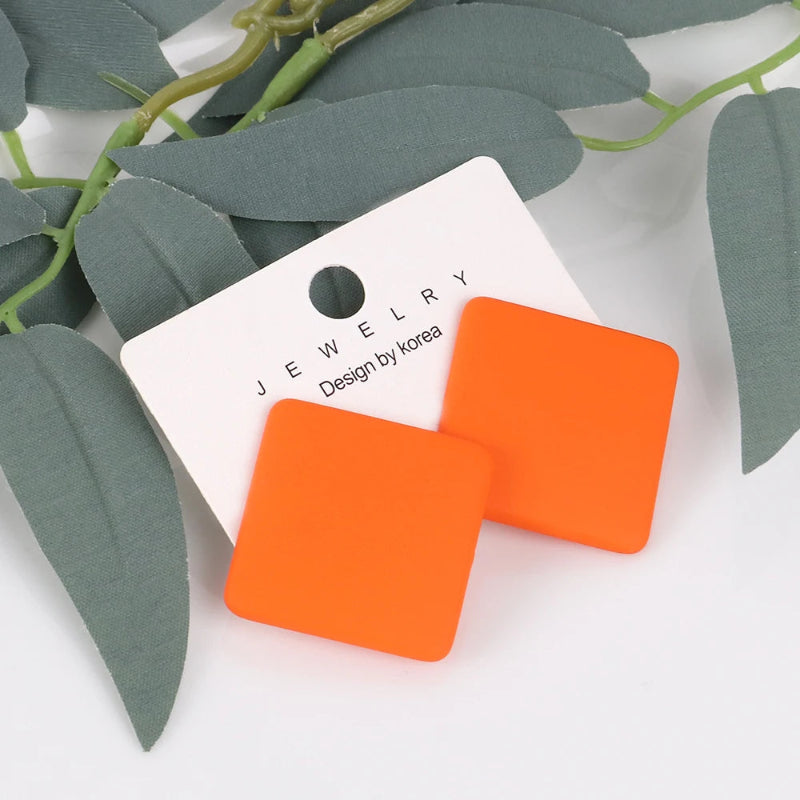 Orange square earrings on a white jewelry card with green leaves in the background