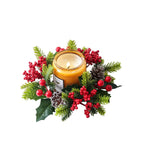 A lit candle in a clear glass jar surrounded by a festive holiday wreath with red berries, green pine branches, pinecones, and holly leaves on a white background.