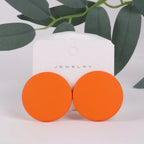 Orange round earrings on a white jewelry card with green leaves in the background