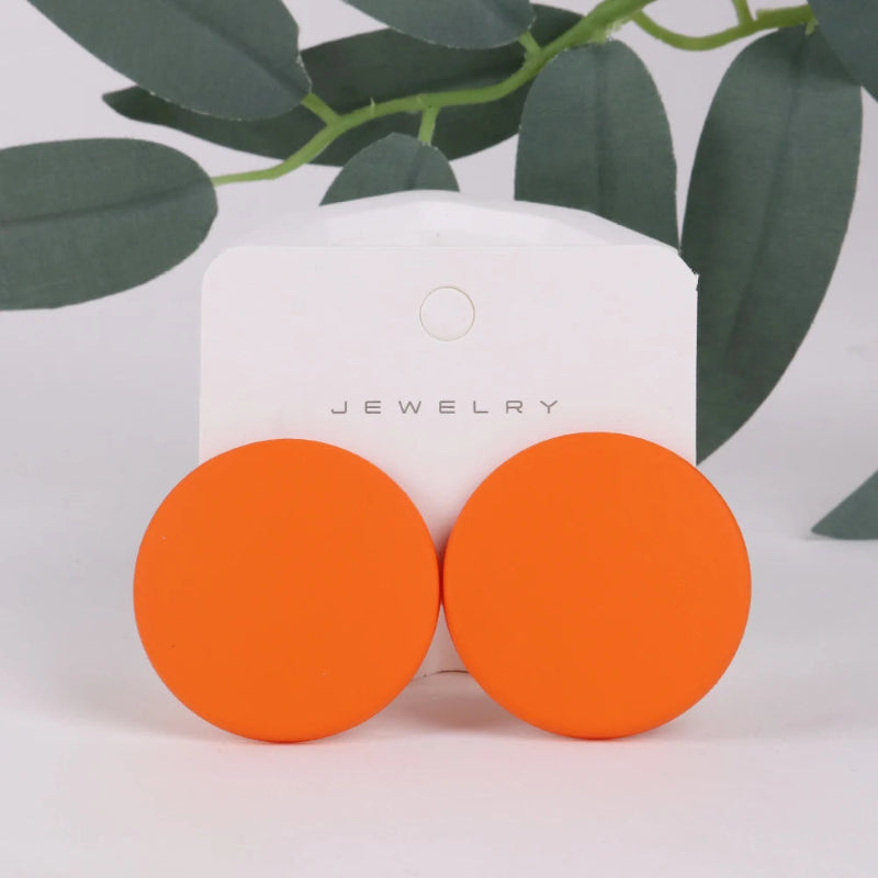 Orange round earrings on a white jewelry card with green leaves in the background