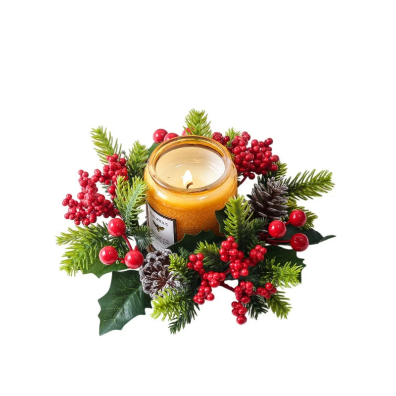 A lit candle in a clear glass jar surrounded by a festive Christmas wreath with green pine branches, red berries, holly leaves, and pinecones on a white background.