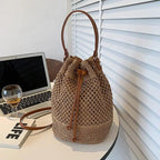 Woven bag with leather straps on a desk next to a laptop and glass of wine.