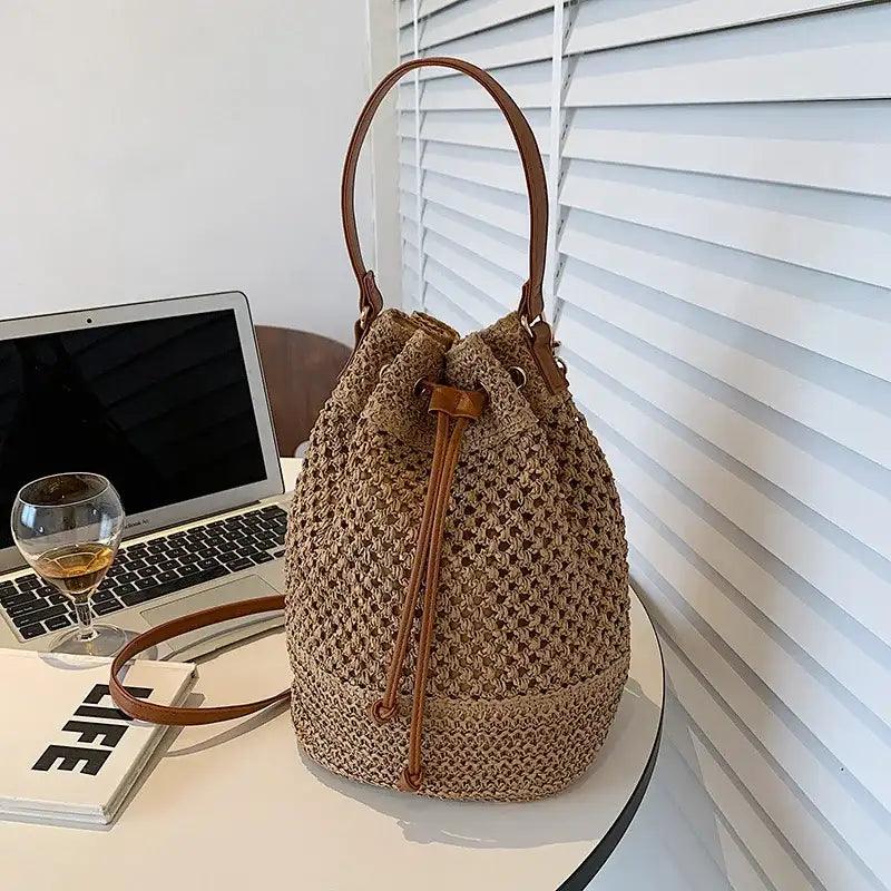 Woven bag with leather straps on a desk next to a laptop and glass of wine.