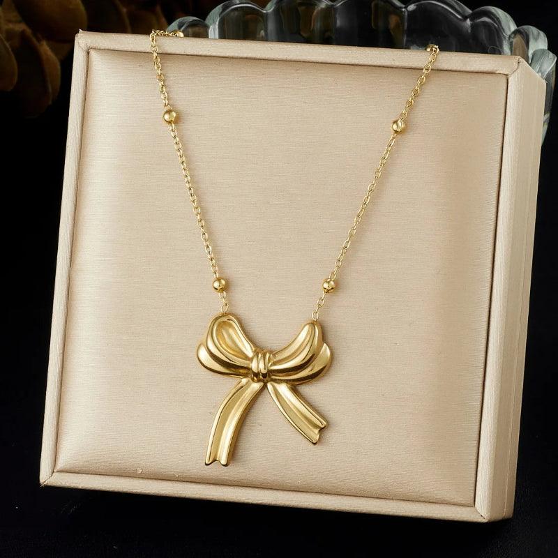 Gold bow-shaped necklace on a beige display box